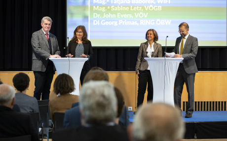 Podium der KEBÖ Jahrestagung © Elisabeth Mandl Hinter zwei Stehtischen stehen jeweils ein Mann und eine Frau, alle lächeln.