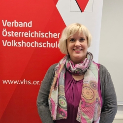 Barbara Brunmair vor der Fotowand des Verband Österreichische Volkshochschulen