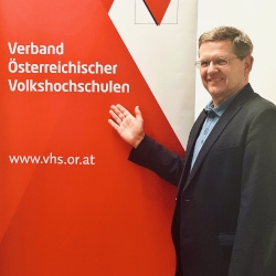 Christian Deutsch vor der Fotowand des Verband Österreichische Volkshochschulen