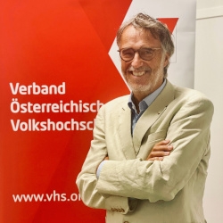 Gerwin Müller vor der Fotowand des Verband Österreichische Volkshochschulen