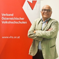 Günter Kotrba vor der Fotowand des Verband Österreichische Volkshochschulen
