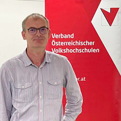 Peter Zwielehner vor der Fotowand des Verband Österreichische Volkshochschulen