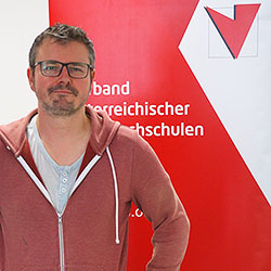 Severin Brunner vor der Fotowand des Verband Österreichische Volkshochschulen