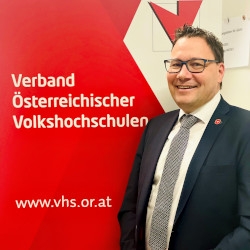 Mag. Stefan Fischnaller vor der Fotowand des Verbandes Österreichischer Volkshochschulen