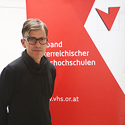 Stefan Vater vor der Fotowand des Verband Österreichische Volkshochschulen